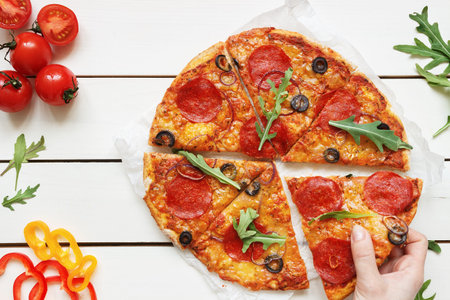 Eating pizza, top view. Hand taking slice of hot delisious pizza on the white wooden table.