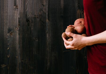 Organic vegetables. Hands holding fresh potatoes. Black wooden background with copy space.の写真素材