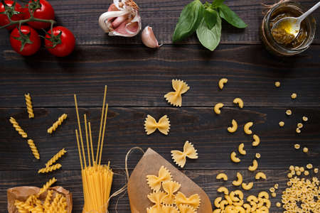 Dried mixed pasta and vegetables on the dark wooden table top view.の写真素材