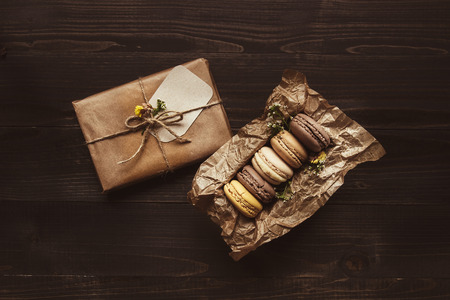 Delicious chocolate macaroons and gift on the wooden table, top view.の写真素材