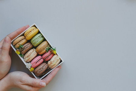 Hands holding gift box with delicious macaroons on the light blue background with copy space, top view.の写真素材
