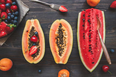 Summer background. Fresh juicy berries, watermelon and papaya on the black wooden table, top view.の写真素材