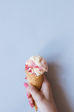 Hands holding pink ice-cream on the blue background, top view.