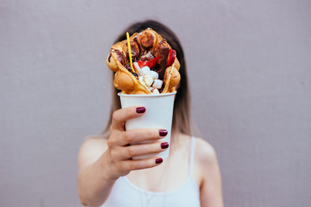 Young woman holding bubble waffle with fruits, chocolate and marshmallow, selective focus.の写真素材