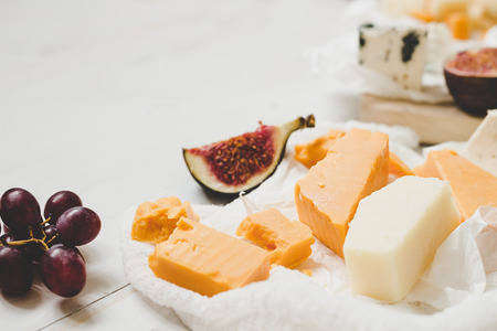 Various types of cheese with fruits on the wooden white table with copy space. Selective focus.の写真素材