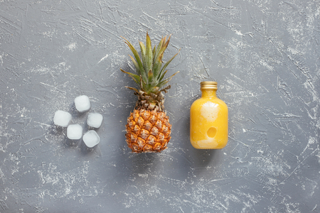 Refreshing yellow smoothie with pineapple and ice cubes on gray wooden table, top view.の写真素材