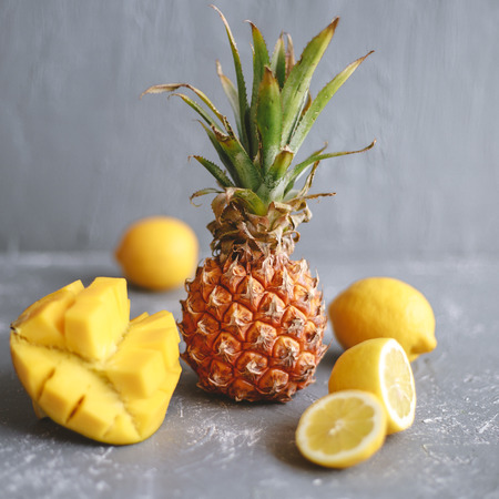 Yellow fruits. Ripe juicy pineapple with mango, banana and lemons on gray wooden table.の写真素材