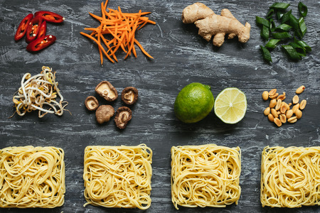 Ingredients for asian dish. Dried asian noodles with lime, nuts, cilantro and vegetables on wooden background. Top view.の写真素材
