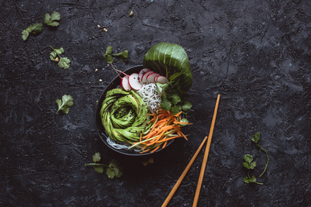 Rice noodles bowl with carrot, cucumber, radish and avocado on black background. Top viewの写真素材