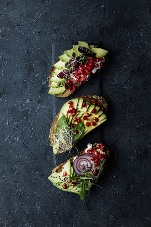 Avocado toasts with avocado slices, seeds and sprouts on dark backgroundの写真素材