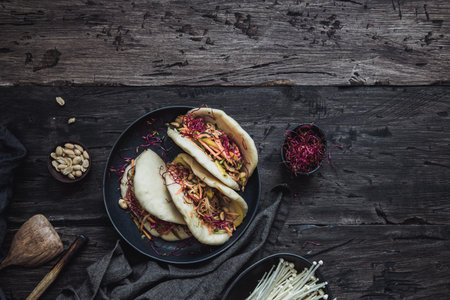 Steamed vegan bao buns with enoki mushrooms, vegetables and peanuts. Dark background with copy...