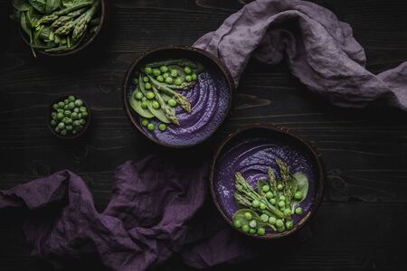 Purple vegetable spring soup with red cabbage, asparagus and green pea on wooden table, top view.の写真素材
