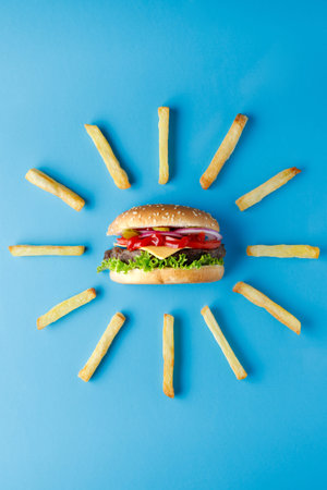 Burger with french fries laid out around on blue backdrop. Creative colorful burger