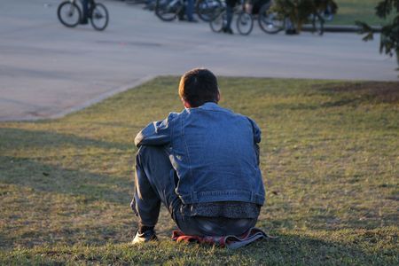 Young man sits on a grass and observesの写真素材