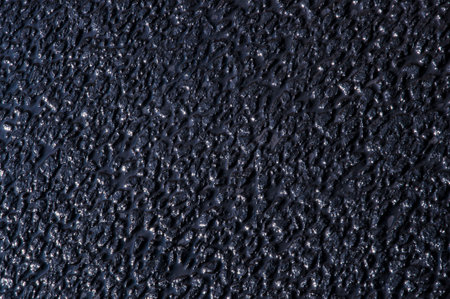 Texture of a wet asphalt road with cracks close-up of a dark blue shade
