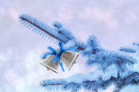 Stylized beautiful spruce branches with snow with white bells on an abstract background with bokeh