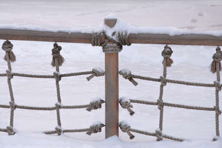 Snow-covered fence made of wooden beams and ropes against the background of snowdrifts in the parkの写真素材