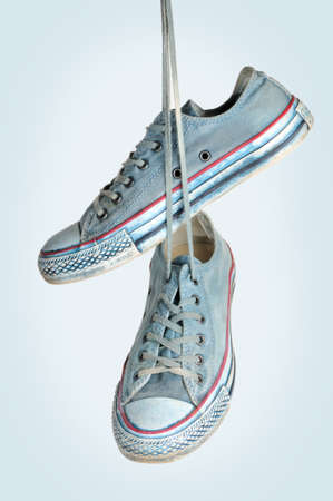 Pair of blue sneakers hangs on the laces on a blue background の写真素材