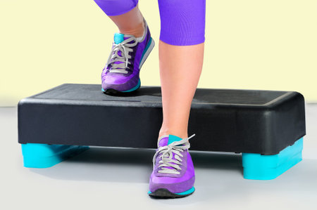 Female feet in violet sneakers do exercise on a black-turquoise fitness aerobic stepper. Front view.