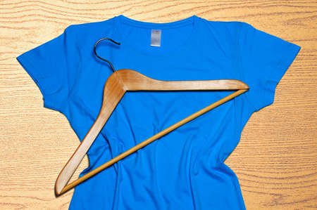 The blue women's t-shirt and wooden hanger lie on a wooden background.の写真素材
