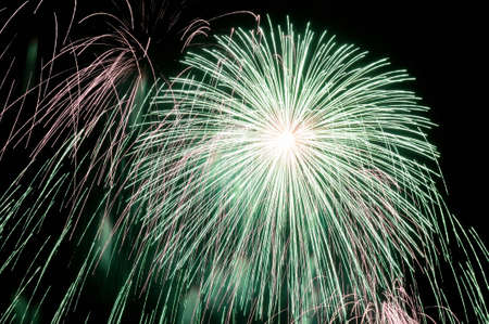 Flashes of green white and pink holiday firework against the black sky.の写真素材
