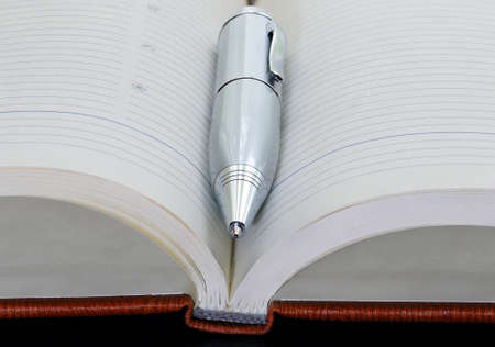 Silver metal pen on the opened notebook on black background. Close-up.の写真素材
