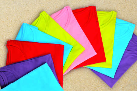Turquoise, light blue, green, red, pink women's t-shirts lie on a beige backgroundの写真素材