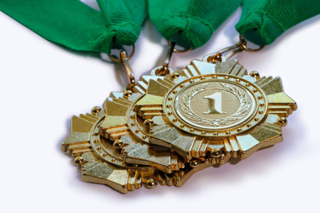 Metal medals of gold color for winners for the first place with ribbons of green color lies one on another isolated on a white backgroundの写真素材