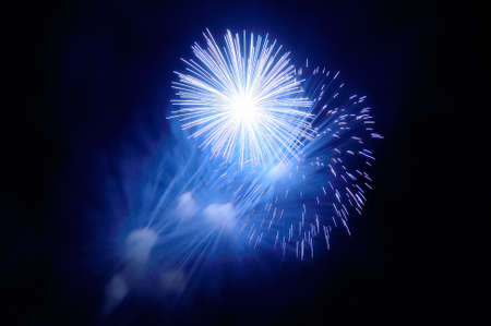 Flashes of blue and white fireworks and blue smoke against the black skyの写真素材