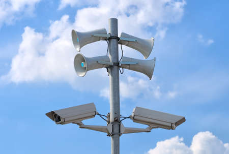 CCTV security cameras and loudspeakers against blue sky with white cloudsの写真素材