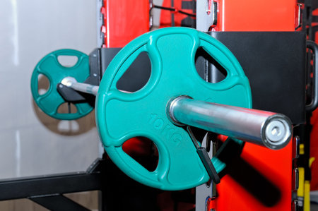 Barbell with green barbell plates with an inscription of 10 kg on a metal rack on a sports, fitness...