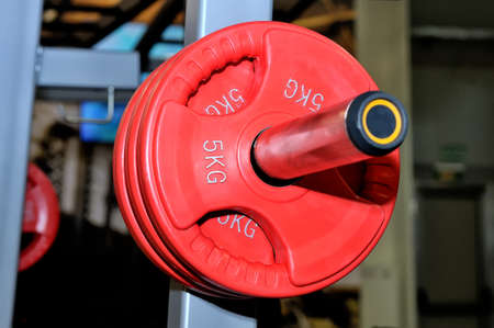 Red barbell plates with an inscription of 5 kg on a metal rack on a dark background in a sports, fitness club. Close upの写真素材