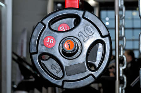 Black barbell plates with an inscription of 10 kg on a red metal rack on a dark background in a sports, fitness club. Close upの写真素材