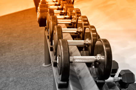 Row of black metal dumbbells on rack in the gym, sport club. Weight training equipment.Selective toned imageの写真素材
