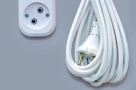 White electric socket and electric wire extension with a plug isolated on a gray background