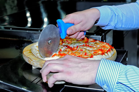 Men's hands cut pizza using a roller knife for pizzaの写真素材