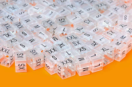 Various plastic clothing size tags, plastic size labels for hangers of clothing store with indexes of the XXS, XS, S, M, L, XL, XXL sizes on a orange background. Small depth of sharpness. Close up.の写真素材