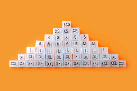 Various plastic clothing size tags, plastic size labels for hangers of clothing store with indexes of the XXS, XS, S, M, L, XL, XXL sizes on a orange background. Close up.の写真素材