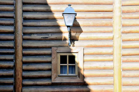 The wall of the ancient wooden house from logs with a window and a streetlight, a half of a wall in a shadow, a half of a wall is brightly litの写真素材