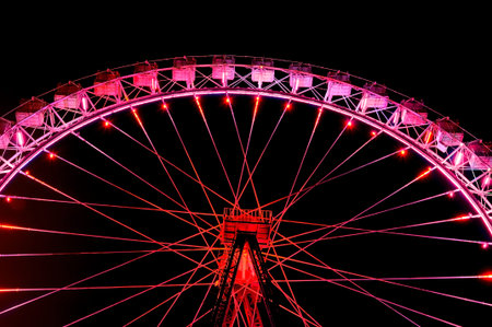 Amusement park at night - big ferris wheel with festive red illumination against dark night sky.