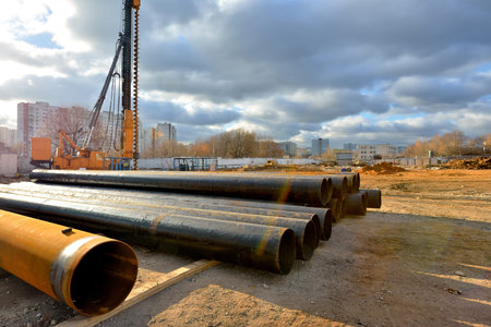 Pile driving machine and metal pipes on a construction site.