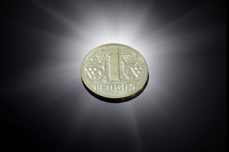 Ukrainian one hryvnia coin on a black background and a flash of light from behind