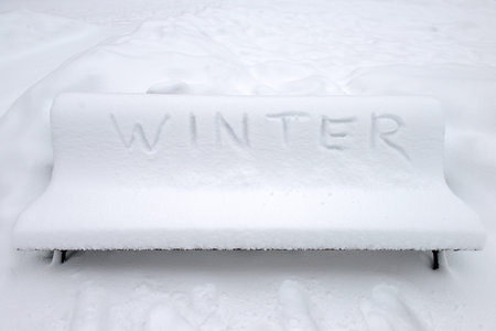 Park bench covered with snow and written Winter in English. Winter concept