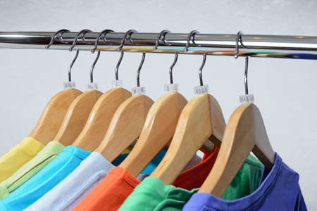 T-shirts of different colors hang on closing rack on wooden hangers with plastic size tagsの写真素材