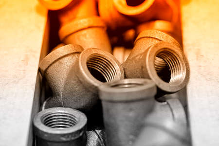 Metal sanitary tees, adapters for water supply pipes lie in a pile. Shallow depth of field. Red toned imageの写真素材