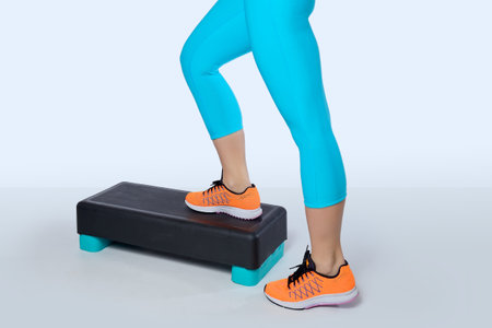 Woman in orange sneakers and turquoise sportswear do exercise on a black-turquoise aerobic and...
