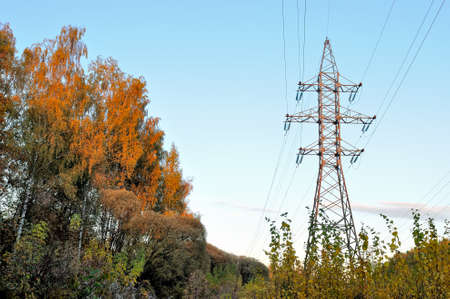 High voltage support, electricity transmission pylon surrounded by trees with yellow autumn foliage.の写真素材