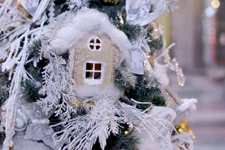 Ñardboard beige toy house decorated with cotton and Christmas toys hanging on Christmas and new year tree. Close-up.の写真素材
