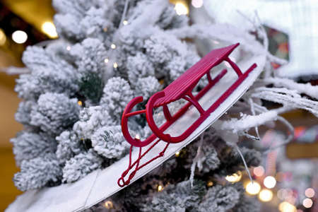 Red toy sled like Christmas toys on a New Year and Christmas tree on a blurry background with bright festive lightsの写真素材