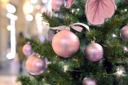 Pink Christmas balls on Christmas tree on a blurred background with bright festive lightsの写真素材